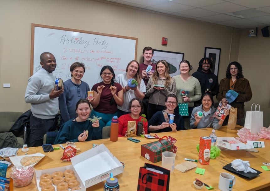 A group of 13 people holding gifts in a conference room